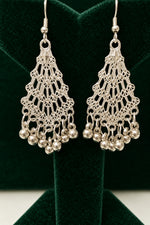A pair of silver-toned filigree dangle earrings with small hanging beads, displayed on a black jewelry stand against a black background.