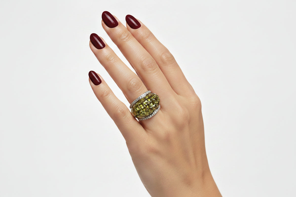 Close-up shot of a hand wearing The Celestial Radiance American Diamond Cocktail Ring, featuring a large oval peridot green checkerboard-cut gemstone set between sparkling silver-toned accent bands.
