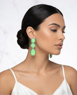 The earrings feature a vibrant, shimmering lime-green iridescent finish with geometric cushion-cut and teardrop-shaped stones in a silver-tone setting.