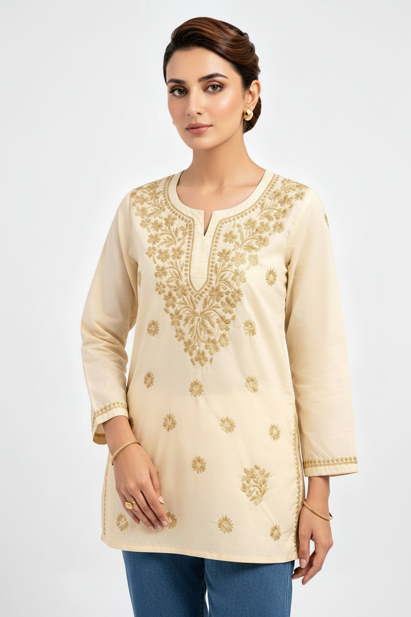 Front view of a model wearing a beige cotton short kurti featuring intricate gold embroidery on the yoke and scattered floral motifs, a keyhole neckline, and a square hem line, styled as a standalone short kurti without bottom wear.