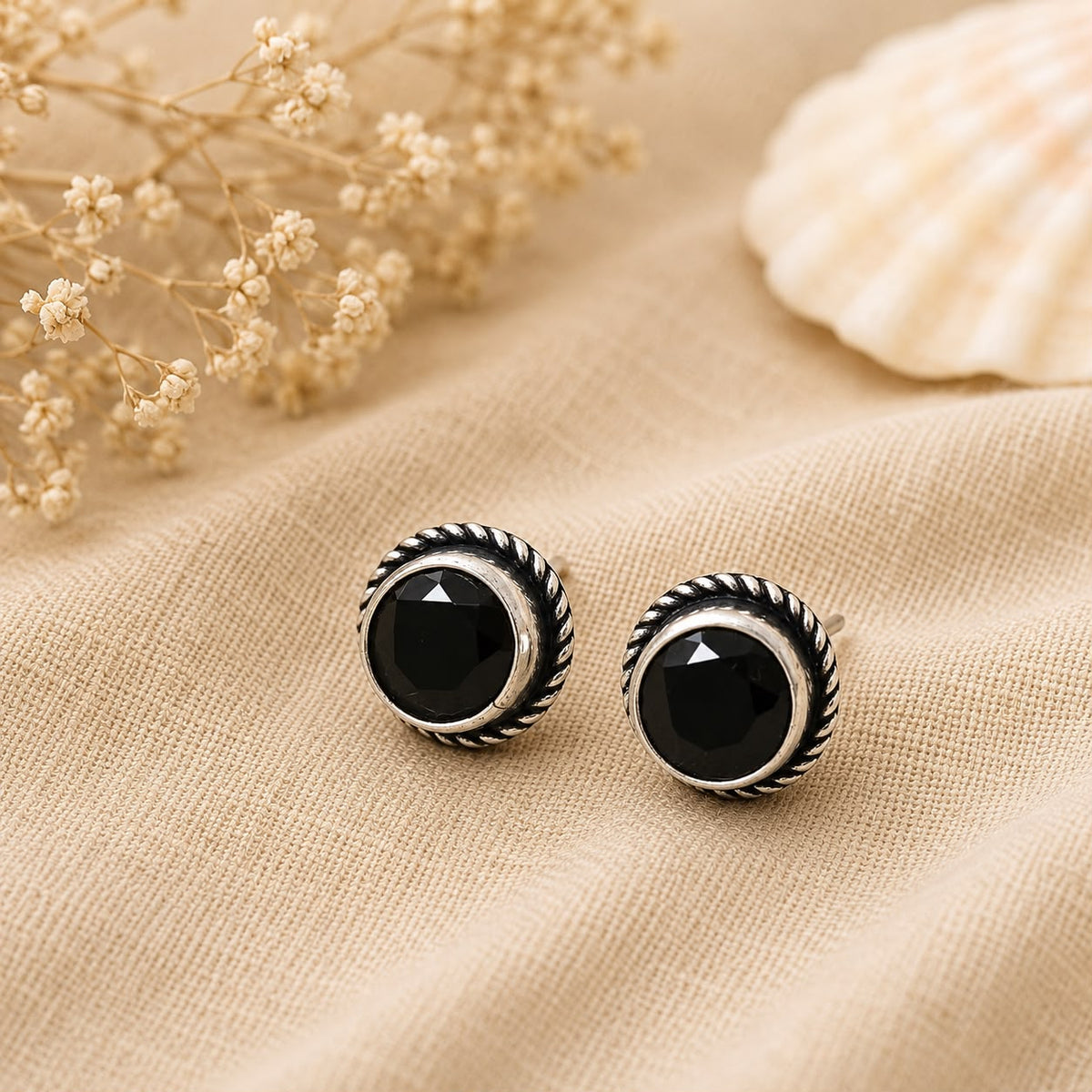 Black stud earrings with silver detailing on a beige fabric background.