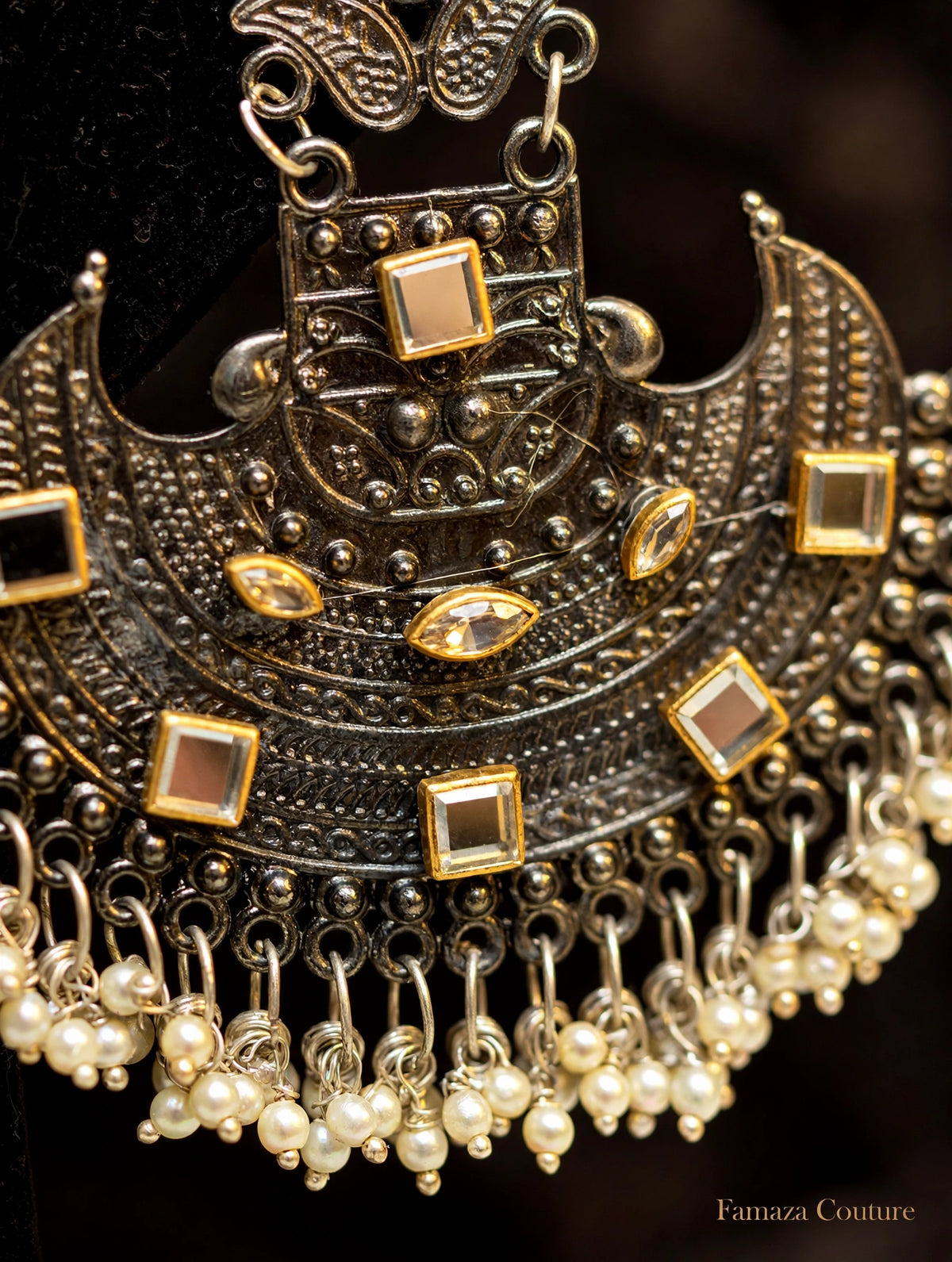An ornate silver-toned traditional necklace with gold accents, square and oval clear stones, and dangling pearl bead chains, shown in a close-up shot against a dark background.