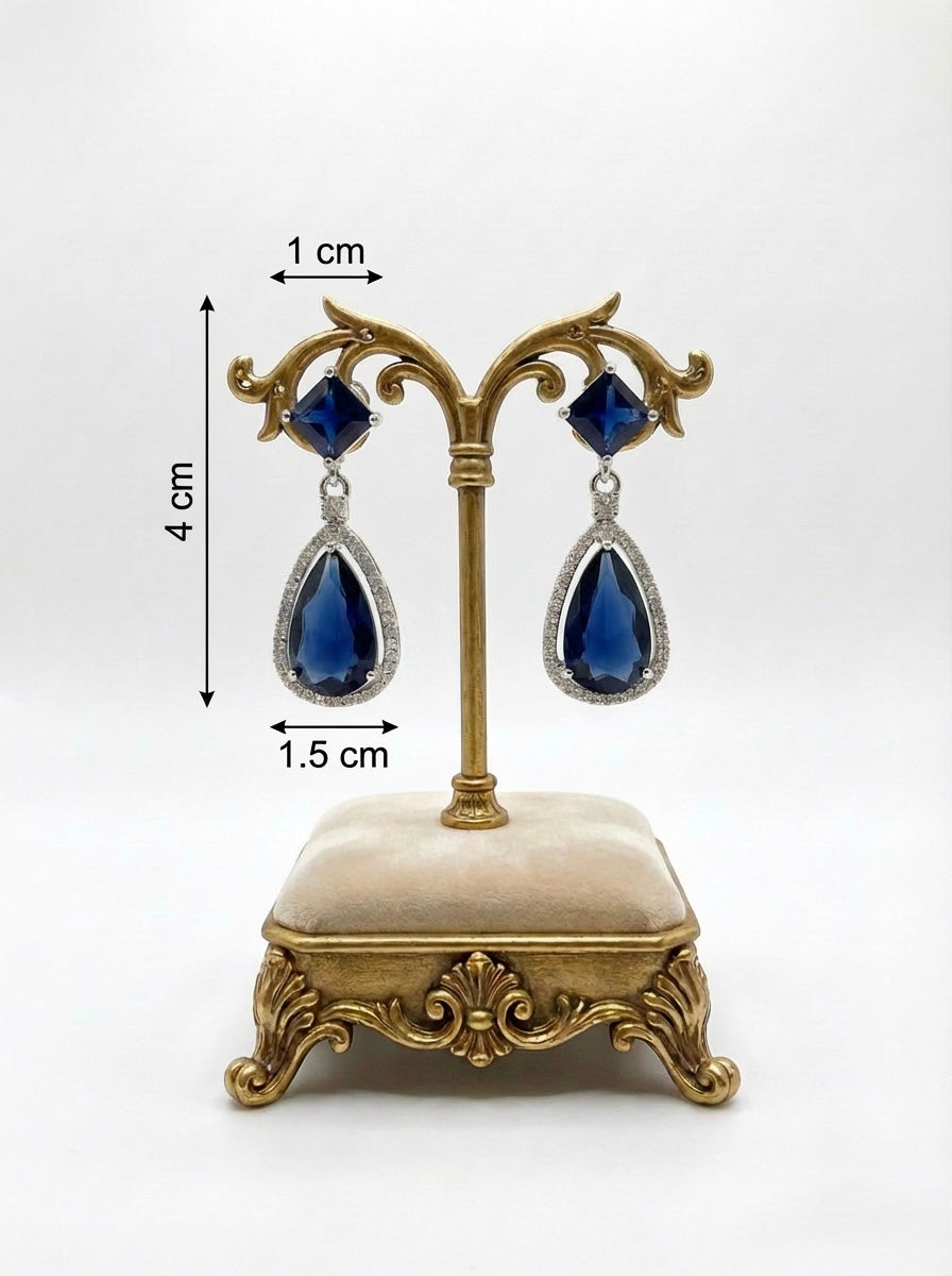 Blue teardrop earrings on a decorative stand with measurements.