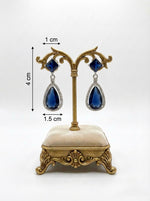 Blue teardrop earrings on a decorative stand with measurements.