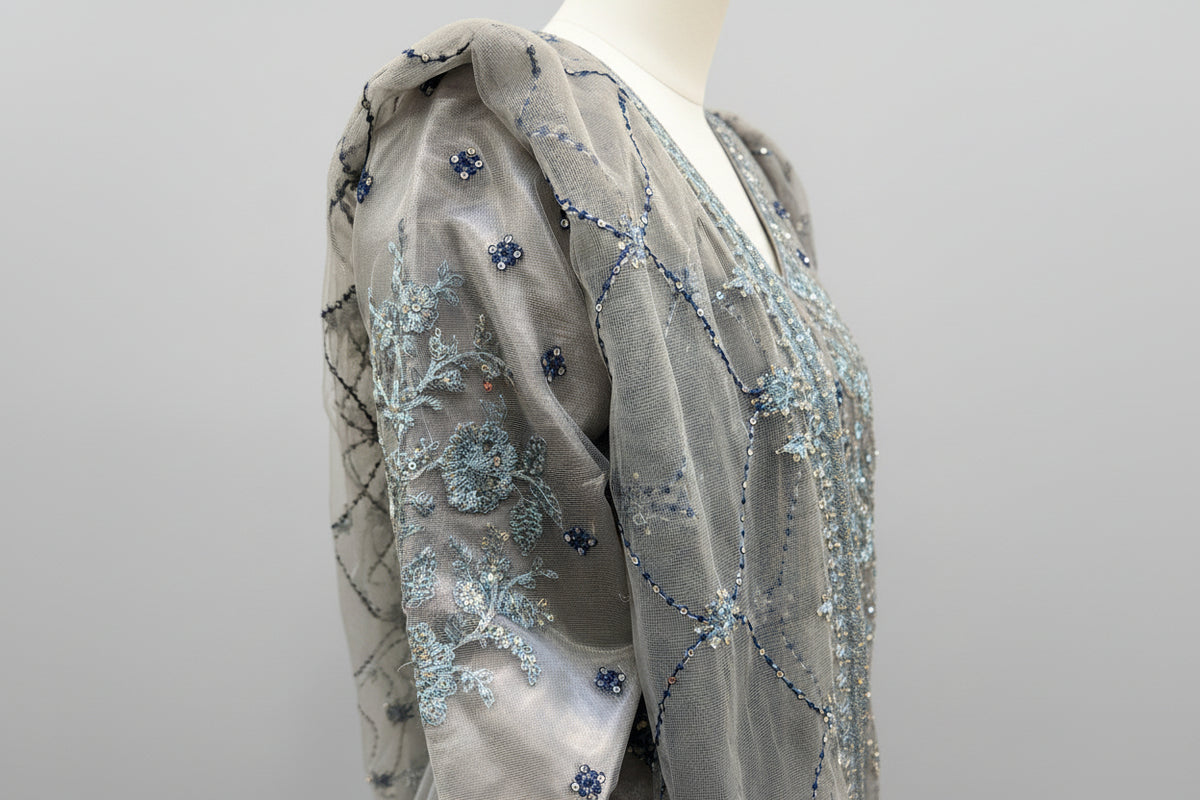 Close-up of a grey fabric with blue embellishments on a mannequin.