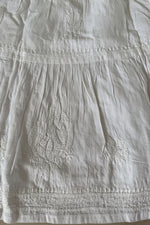 Close-up of a white embroidered fabric garment, showing textured embroidery and gathered seams.