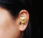Close-up of a woman’s ear featuring a petite gold-plated lotus ear climber. The small, detailed flower sits centrally on a vertical bar that extends from the upper helix to below the lobe. Dark hair frames the ear against a simple, dark background.