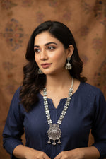 Close-up of a woman wearing a heavy oxidised long necklace with a large floral pendant and matching jhumka-style earrings.
