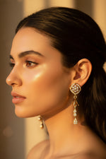 Close-up of rose gold bird-motif earrings featuring white stones and a tiered bell drop.