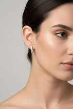 Close-up of the 1.5cm Lumi silver AD earrings featuring a curved stone-set bar and a dangling teardrop stone.