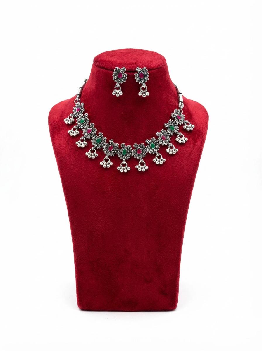 Close-up of the handcrafted floral motifs in oxidised silver featuring teardrop-shaped red and green gemstone accents.