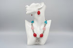 Colourful beaded necklace with red, pink, and blue beads on a black stand.