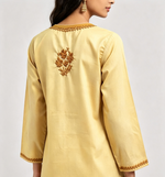 Back view of a model wearing a creamy beige short kurti showcasing detailed embroidery along the upper back neckline and a centered floral motif on the upper back.