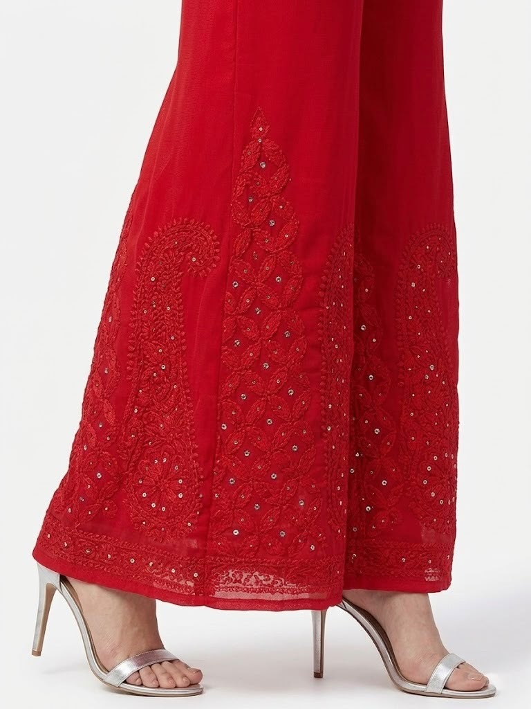 Side view of a crimson sharara featuring detailed Akhandani embroidery and delicate embellishments along the hem, set against a pure white background.