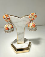 A pair of handcrafted Kalamkari art-printed jhumka earrings displayed on a white marble and gold-trimmed stand against a clean light background.