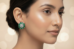 A close-up side profile of a woman wearing a green and white floral stud earring against a soft beige bokeh background.