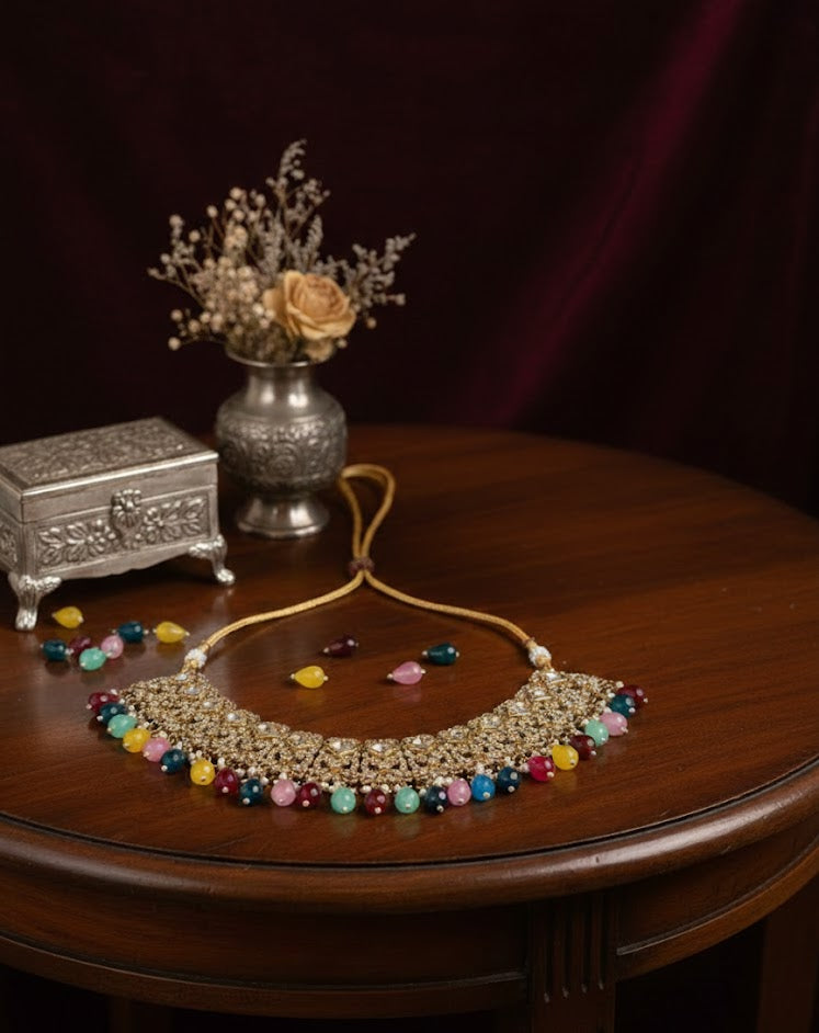 Decorative necklace with colorful beads on a wooden table with a vase and jewelry box in the background.