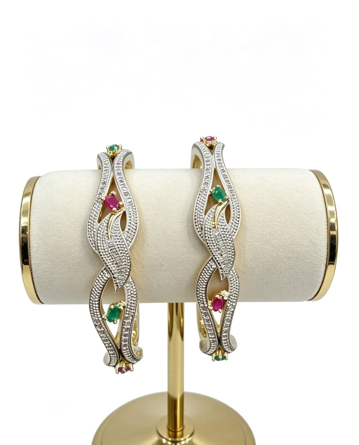 Set of two dual-tone floral lattice bangles featuring white American Diamond pavé settings with alternating ruby and emerald-colored gemstone accents, displayed on a gold-toned jewelry stand.