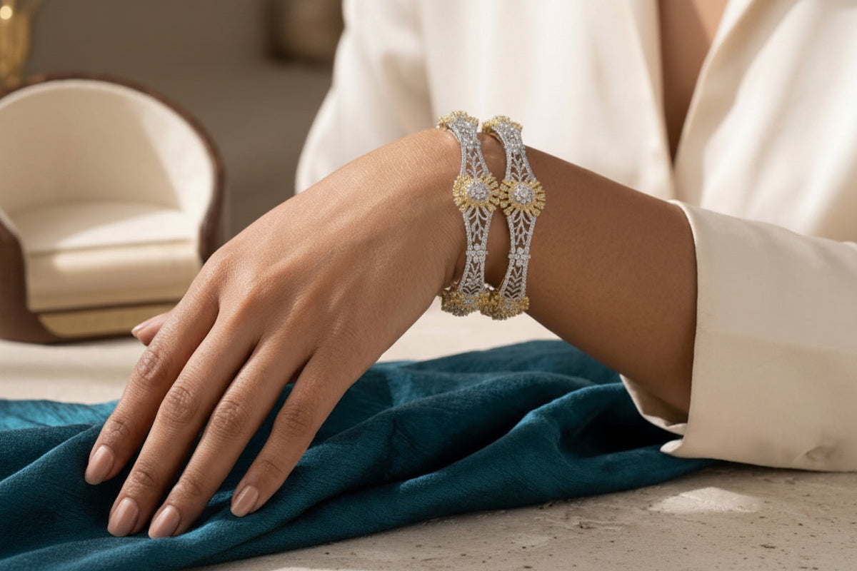 Close-up of a model's hand wearing a pair of dual-tone gold and silver plated bangles featuring intricate filigree jali work and central starburst floral clusters studded with American Diamonds.