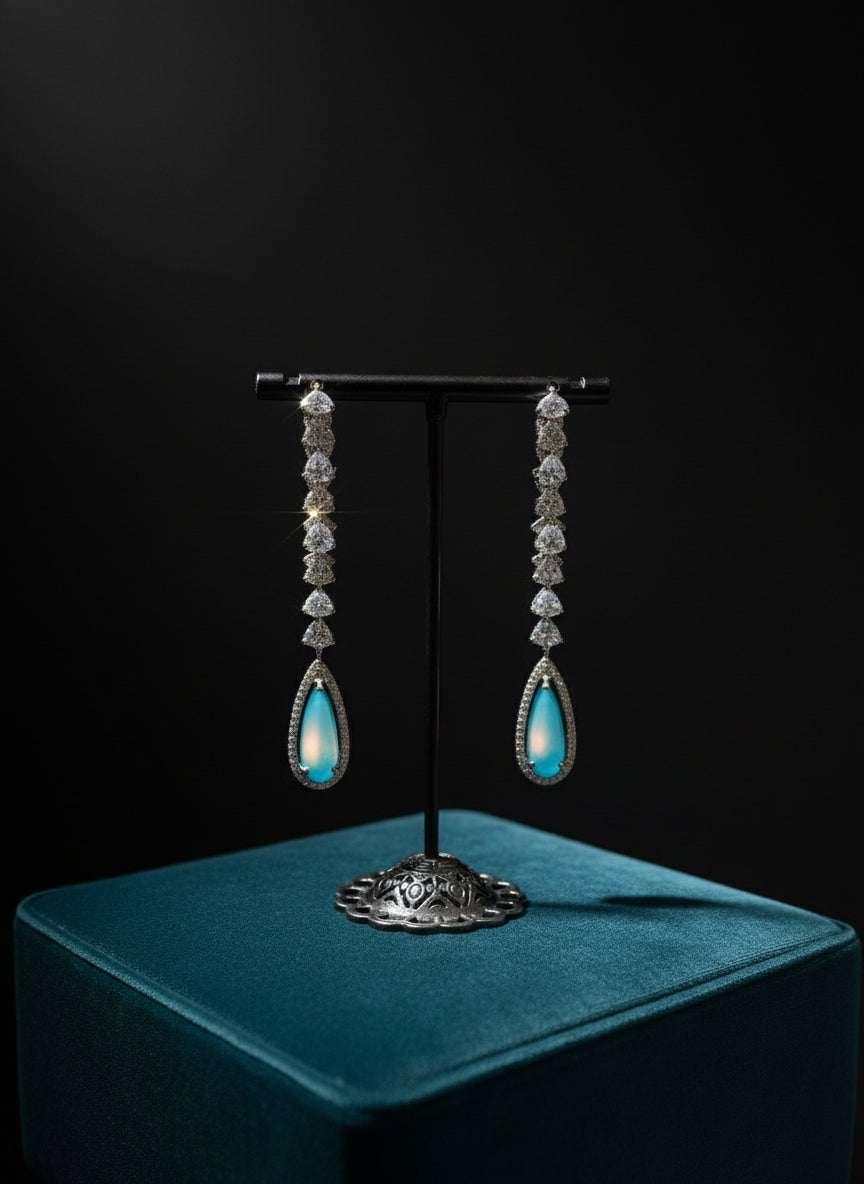 Pair of turquoise teardrop earrings on a stand with a blurred jewelry store background