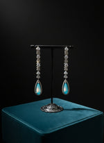 Pair of turquoise teardrop earrings on a stand with a blurred jewelry store background