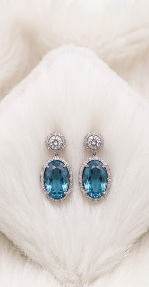 Close-up of elegant oval blue topaz drop earrings resting on a soft white furry cushion.