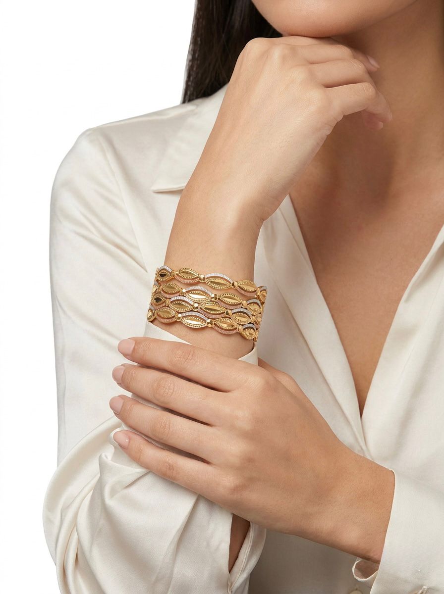 A professional lifestyle image of a woman wearing a set of four three-tone micro gold-plated bangles. The bangles feature an intricate floral lattice and scalloped eyelet design in yellow gold, white gold, and pink gold finishes, styled with a cream silk blouse.