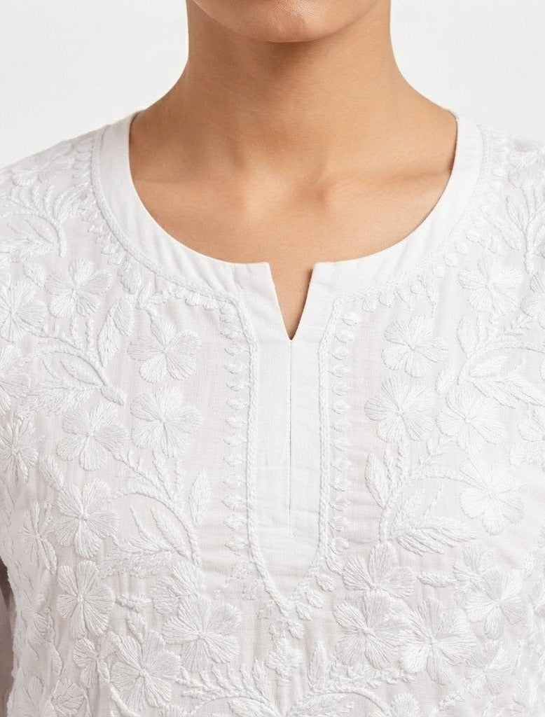 Close-up view of the neckline and chest area of a white cotton short kurti featuring dense, intricate floral white embroidery and a keyhole neckline, styled without bottom wear.
