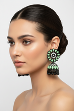 Model is wearing Elegant black brass jhumka earrings featuring a refreshing mint green stone floral stud and matching mint stone inlay on the jhumka dome.