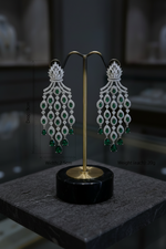 Pair of diamond and emerald earrings on a black stand with a blurred background