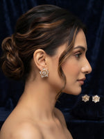 A woman in profile wearing a sparkling floral stud earring, with matching earring pieces displayed on a dark velvet surface in the background.