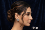 A woman in profile wearing a sparkling silver-toned floral stud earring, with matching earrings displayed on a dark navy velvet surface. The background is a matching dark navy velvet fabric.