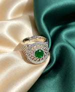 Luxurious silver-tone cocktail ring featuring a round vibrant emerald green centre stone surrounded by marquise and round-cut cubic zirconia accents in an intricate halo setting, with a textured honeycomb-patterned band, displayed on champagne and emerald green satin, premium American Diamond jewellery.