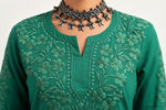 A close-up view of a person wearing a vibrant green short kurti with detailed tonal floral embroidery along the split round neckline, accessorized with an ornate silver-toned choker necklace.