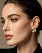 Famaza Couture Radiant Leaflet American Diamond Gold-Plated Studs – Circular gold-toned earrings featuring sparkling American Diamonds, elegant leaflet motif at center surrounded by a halo of clear stones, worn on ear