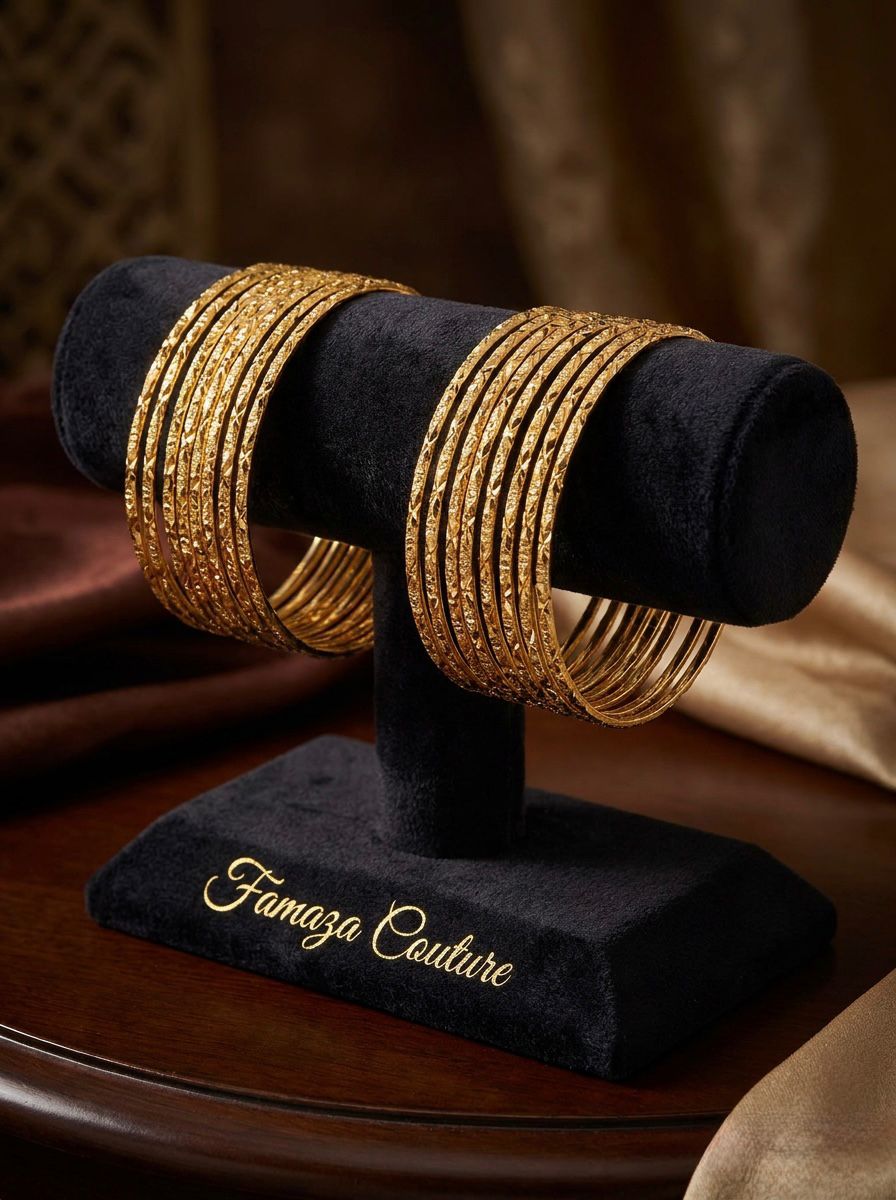 A professional product photograph of 12 sleek, micro gold-plated copper bangles with a diamond-cut texture, displayed on a black velvet Famaza Couture branded jewelry stand.
