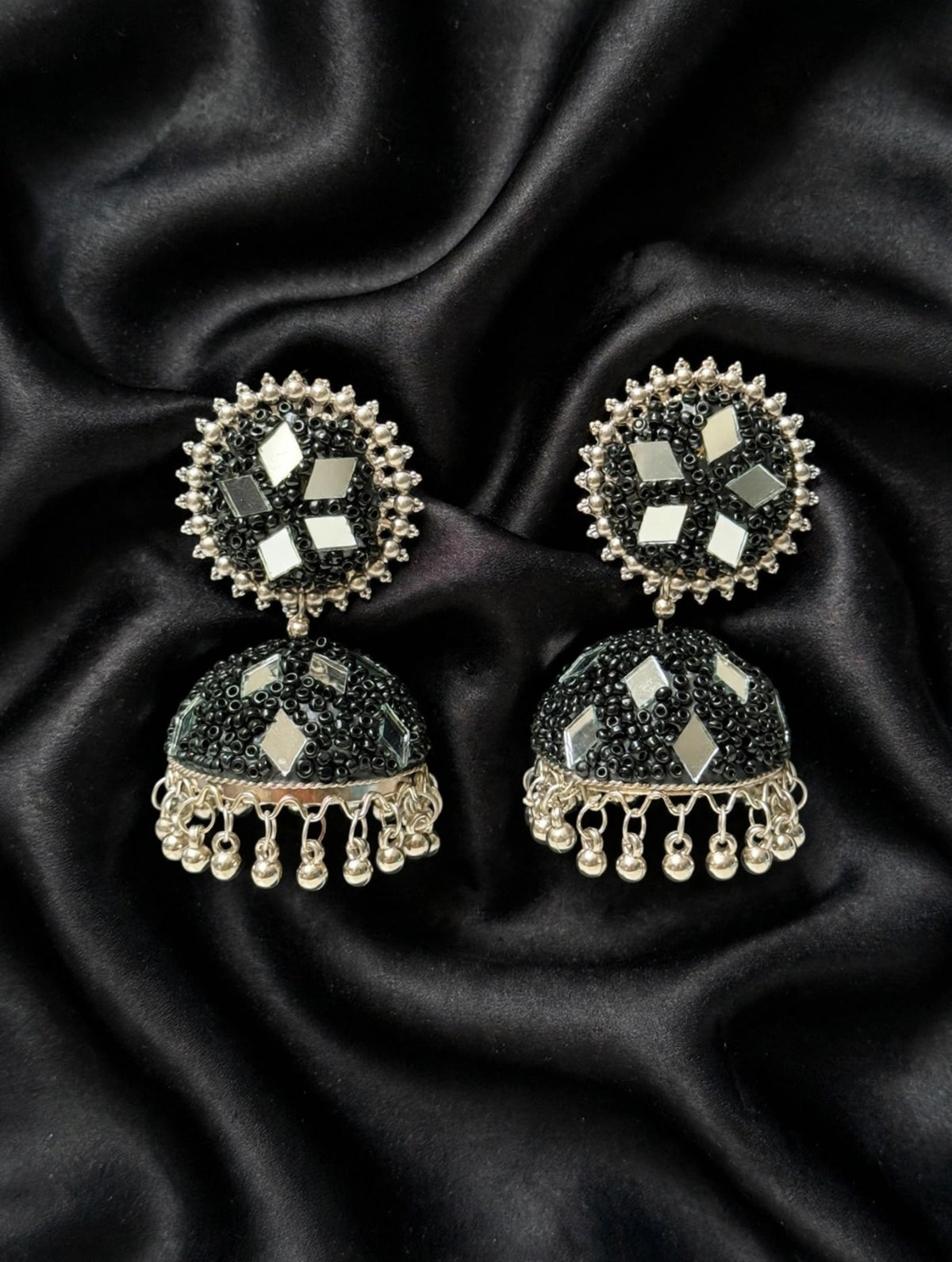 Black mirror bead jhumka — jet black micro-beadwork, multi-tone mirror inlays, polished gold-silver trim & curved ghungroo drops, laid on draped black silk — Famaza Couture.