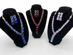Three matching jewelry sets displayed on black velvet busts against a white background. The left set features a silver-tone necklace and earrings with rectangular blue stones.
