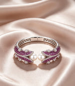 Pearl and purple crystal silver cuff bangle resting on soft champagne satin silk — Famaza Couture luxury jewelry, polished silver-tone open cuff with deep purple stones and luminous white pearls, elegant flat-lay product photography with warm cream fabric backdrop.