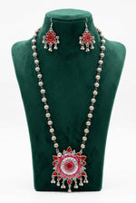 Famaza Couture red hand-painted enamel beaded strand statement necklace with large circular pendant, matching chandelier teardrop dangle earrings, oxidised silver-tone finish, displayed on black velvet bust stand, clean white background.