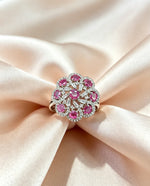 : The Famaza Couture Royal Magenta-Pink Floral Cluster Statement Ring elegantly resting on a soft, glossy fabric backdrop, emphasizing its intricate crystal details and vibrant magenta gemstones.
