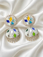 White bead multi-color meenakari jhumka — cobalt blue, golden yellow, turquoise, emerald green geometric patches, silver mirror inlays, gold-tone ghungroo drops, laid on soft draped white silk — Famaza Couture.