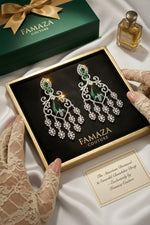 Famaza Couture dangle earrings displayed in an open presentation box, with lace-gloved hands holding the box, a branded green gift box, a small perfume bottle, and a card on a dark marble surface.