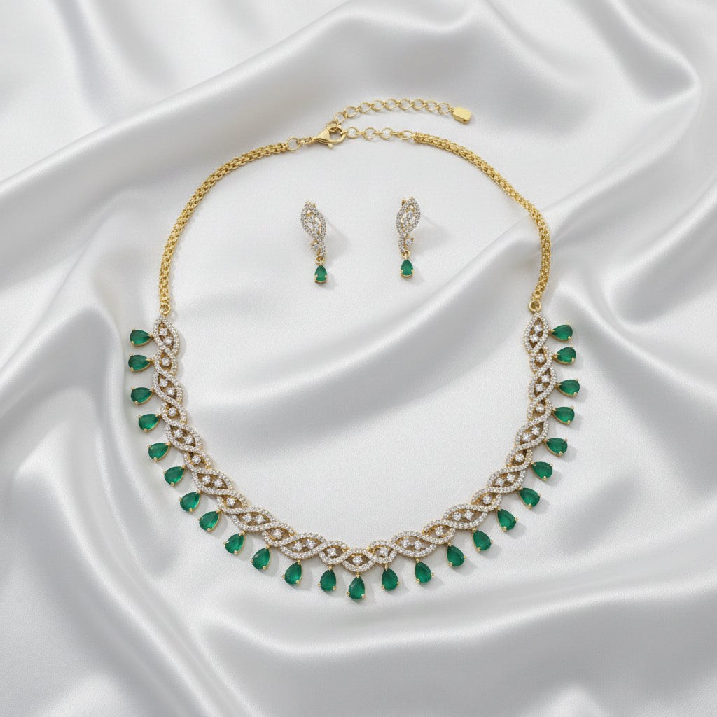 Gold necklace and matching drop earrings with green teardrop gemstones and white stone accents, displayed on a gray jewelry box.