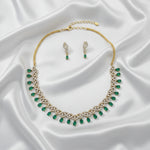 Gold necklace and matching drop earrings with green teardrop gemstones and white stone accents, displayed on a gray jewelry box.