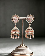 FC Rose Gold Pastel Pink Floral CZ Jhumka Earrings beautifully displayed on a velvet boutique stand against a neutral background.
