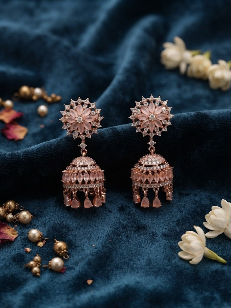FC Rose Gold Pastel Pink Floral CZ Jhumka Earrings styled on a luxurious blue velvet background with jasmine flowers and decorative beads.