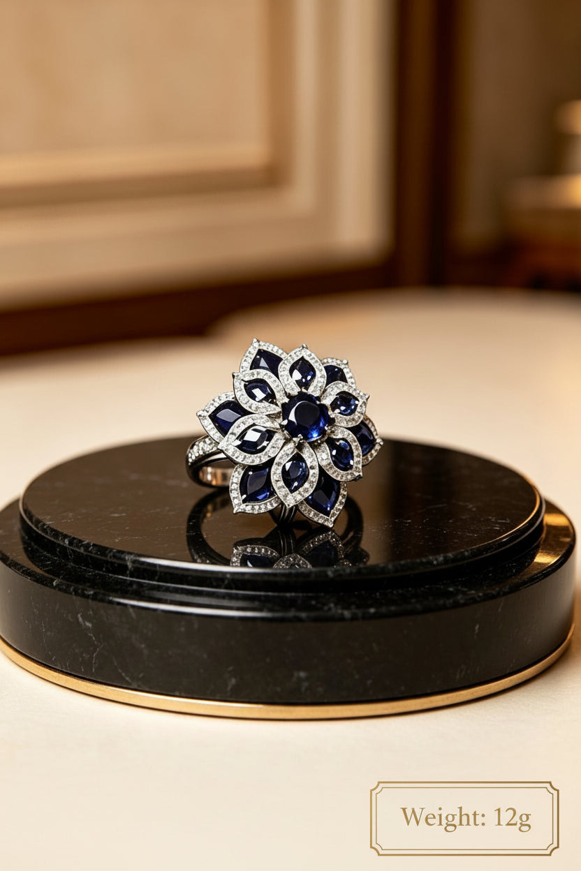 Studio render of the Famaza Couture sapphire and American diamond floral cocktail ring displayed upright on a sleek black luxury stand against a neutral background.