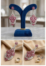 A pair of white gold or sterling silver chandelier earrings with pink ruby floral clusters and diamond accents, displayed on a blue velvet stand in a well-lit jewelry store.