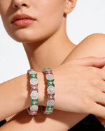Model wearing a pair of silver-tone bangles featuring a floral pattern of pink, green, and clear American Diamonds.